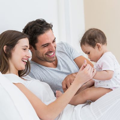Cheerful couple playing with baby girl on bed at home
