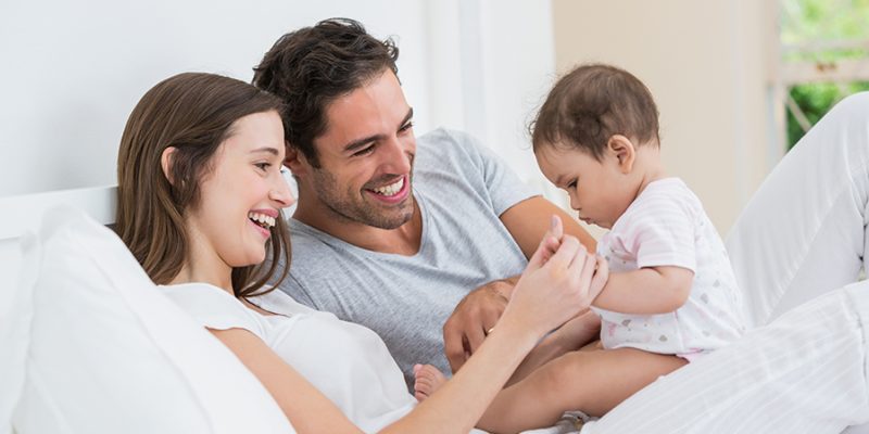 Cheerful couple playing with baby girl on bed at home